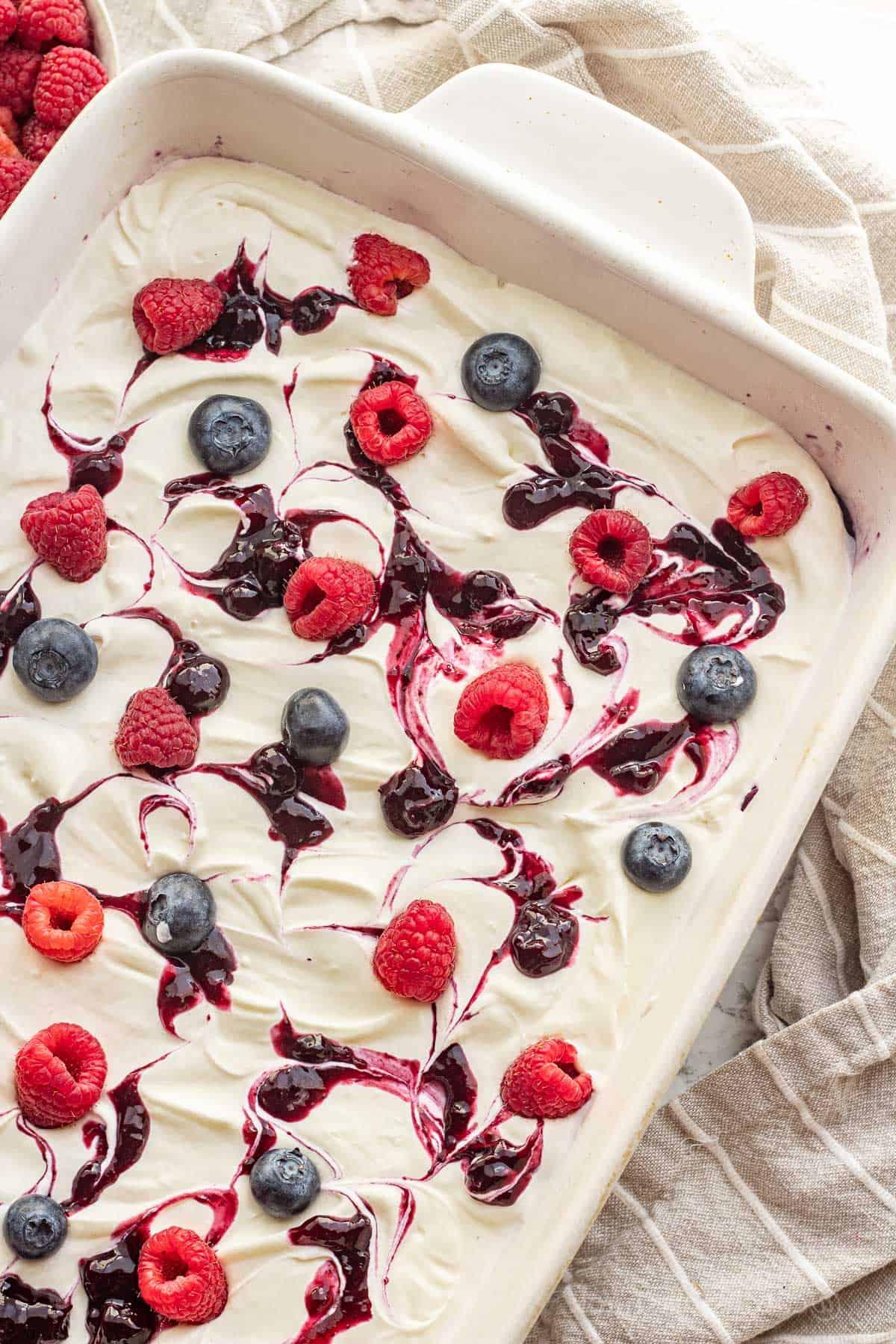 Blueberries and raspberries on whipped filling and blueberry jello in white dish.