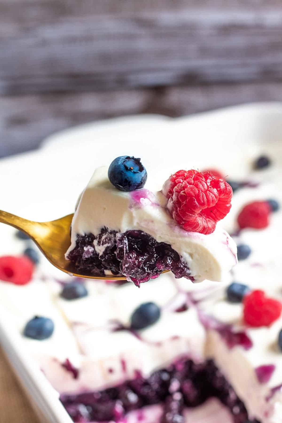 Spoonful of blueberry jello salad with whipped cream cheese topping and berries.