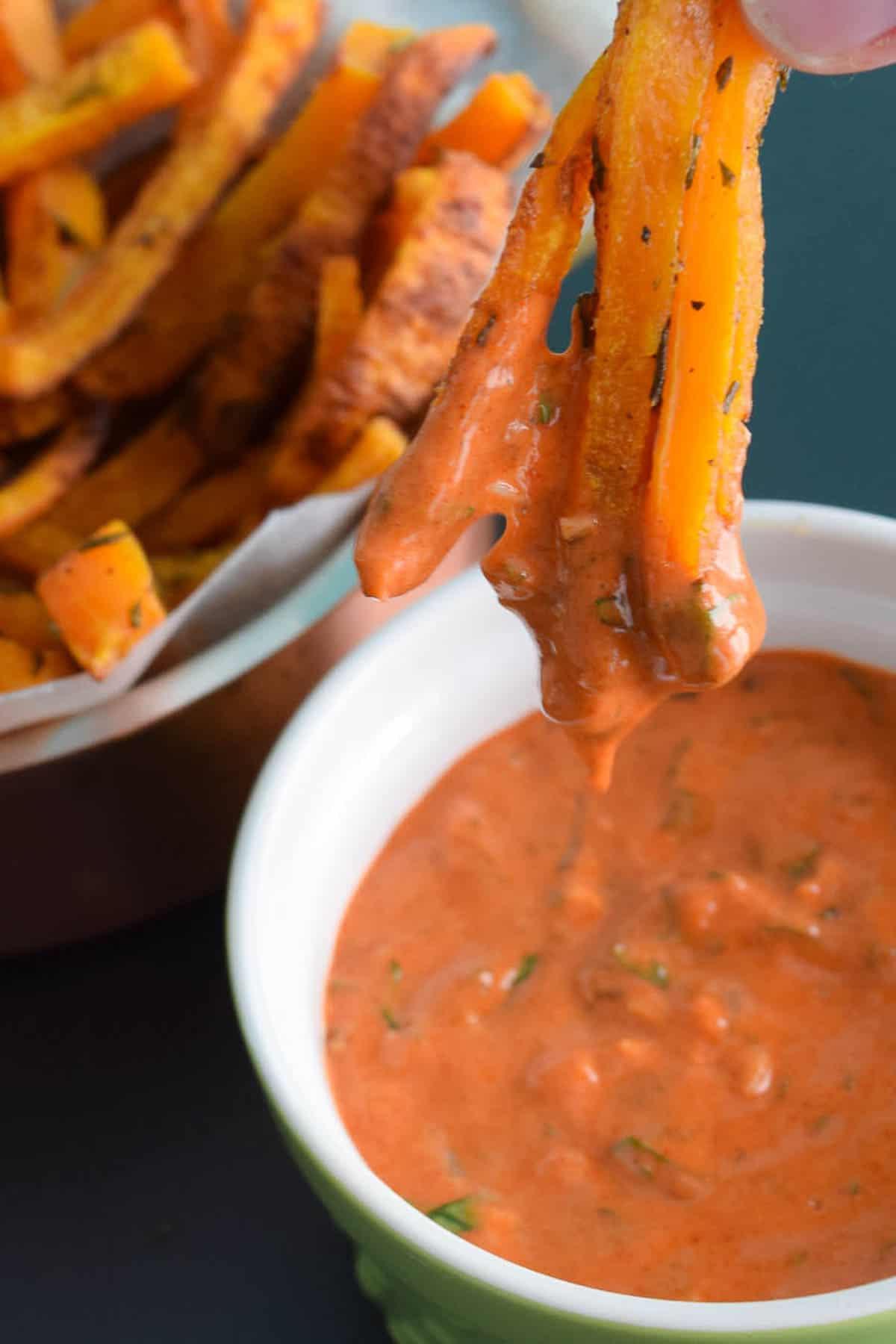 close up view of butternut squash fries being dipped into a red serving sauce