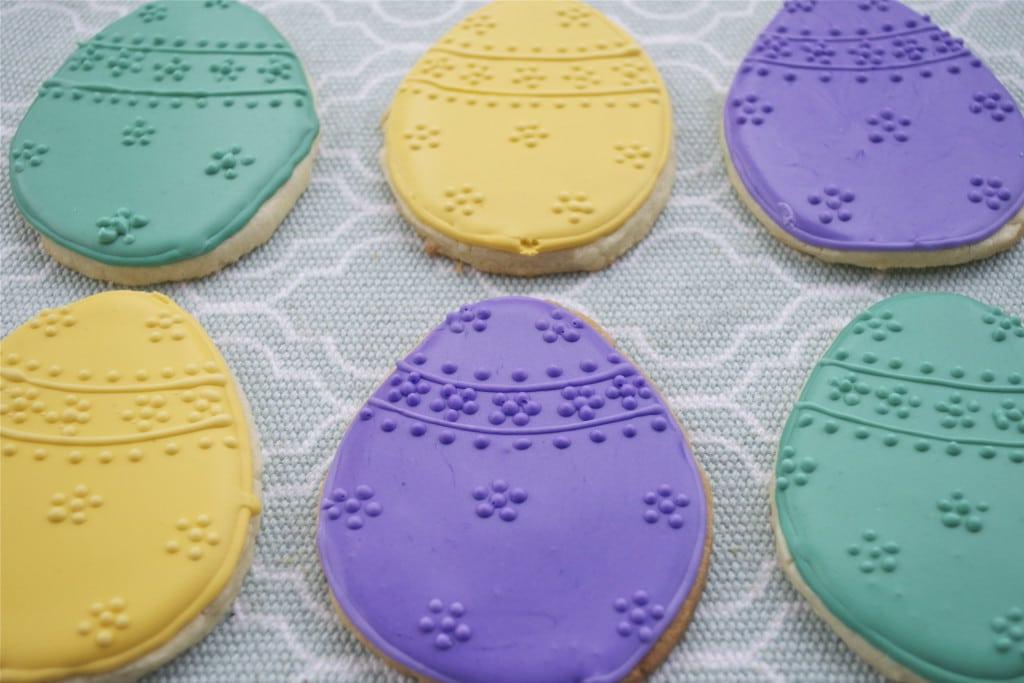Sugar cookies decorated with purple, yellow and green royal icing to look like Eggs with raised dot designs.