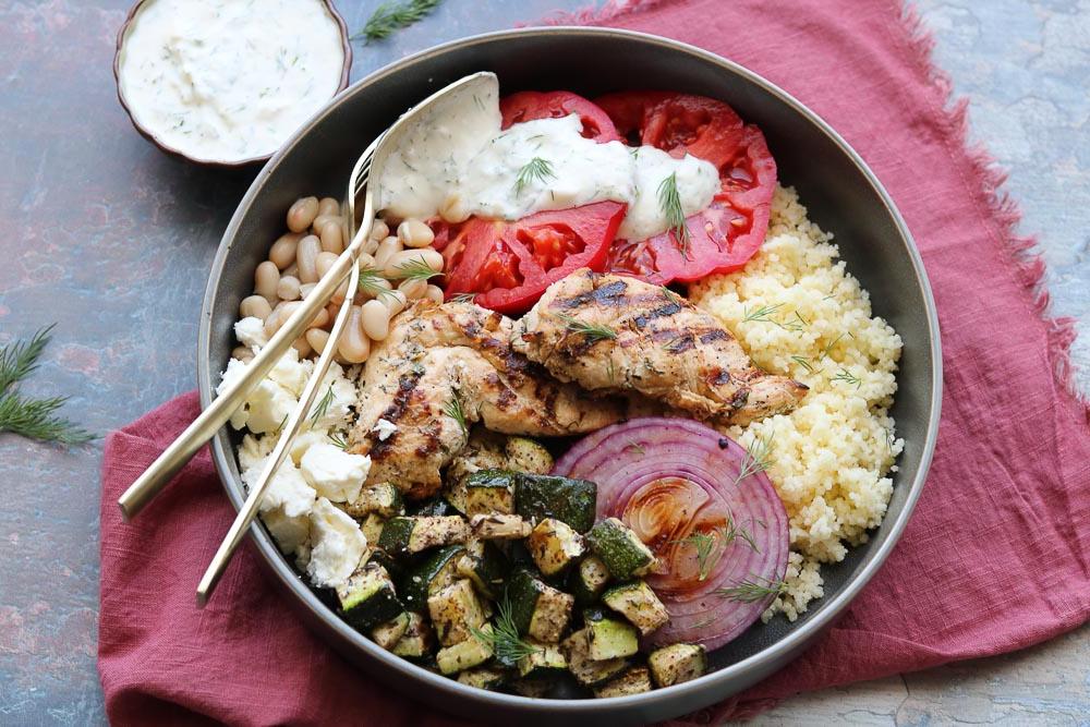 mediterranean grilled chicken bowl with fork on table with napkin and yogurt dill dressing
