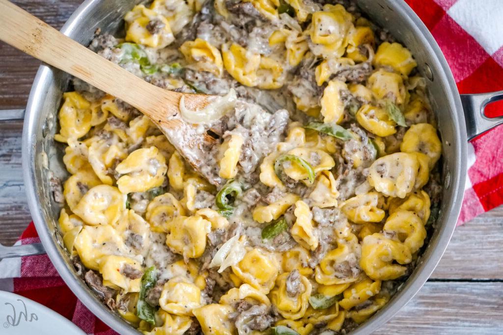 A wooden spoon sits in the sauté pan with the Philly Cheesesteak Tortellini.