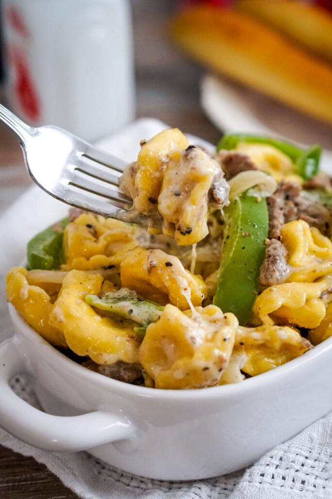A serving of Philly Cheesesteak Tortellini in a white dish being served with a fork.